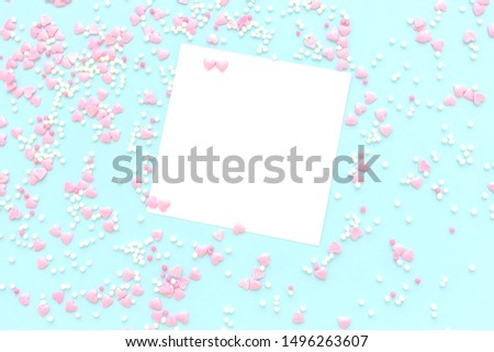 Festive romantic gentle abstract background for the design. Pink confetti in the shape of hearts and blank white sheet of paper for text  on a blue background. Copy space.