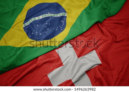 waving colorful flag of switzerland and national flag of brazil. macro