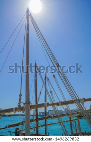 Ropes and spars of traditional rigging of dhow moored along The Corniche, Doha Old Town waterfront with lens flare above mast tip.