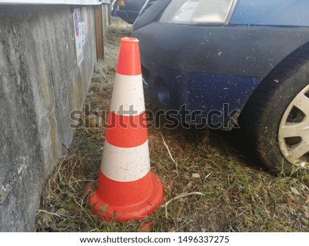 Orange traffic cone near an old car. Signal danger on a street. 