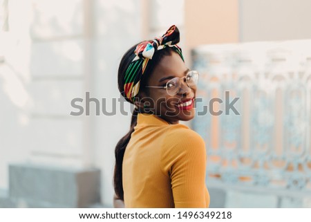 Elegant black girl with glasses, a yellow sweater and a colored headband on the streets of the city.