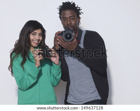 Portrait of young woman and man with digital cameras in studio