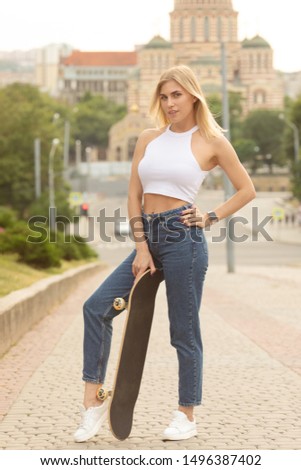 Portrait of smiling young female skateboarder holding her skateboard. Woman with skating board at skate park looking at camera outdoors.