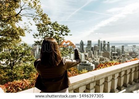 Woman tourist making heart shape with her hands, enjoying panoramic view of Montreal city skyline with modern skyscrapers and famous landmarks. Sending love greetings from Mont Royal