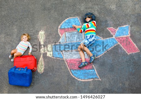 Two little children, kid boy and toddler girl having fun with with airplane picture drawing with colorful chalks on asphalt. Siblings painting with chalk and going on vacations.