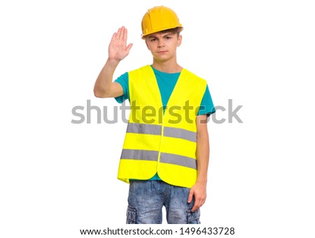 Handsome Teen Boy wearing Safety Jacket and yellow Hard Hat doing stop sign with palm of hand. Portrait of serious Child making stop gesture and Looking at camera, isolated on white background.