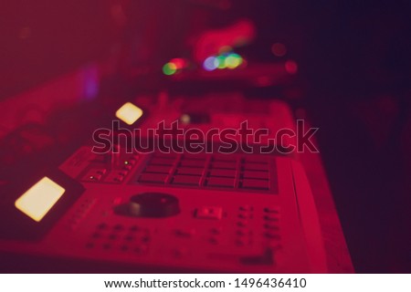 Midi controller for electronic music production.Professional dj audio equipment on concert stage in bright red lights.Push buttons on analog drum machine for hip hop disc jockey.Press key to play mix