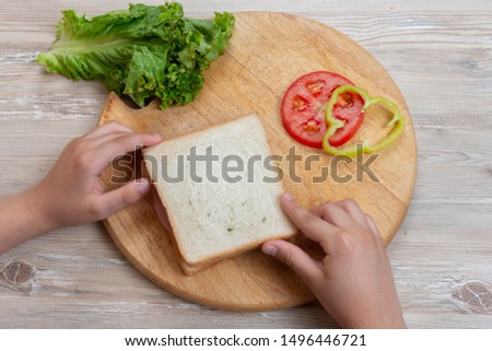 A boy is  preparing a sandwich of meat and vegetables. Breakfast for school.