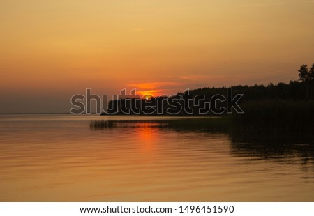 The horizontal photo of golden sunset above the river or sea. Reflection in the water like fire. Seacoast.
