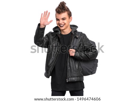 Happy teen boy student with backpack in style of punk goth dressed in black, isolated on white background. Teenager Back to school. Cute child with spooking make-up making greeting gesture with palm.