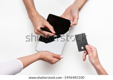 Close up top view of a woman hands over bank card to a man in order to pay for the product. Tablet and pen on a white table. Concept of e-commerce and online shopping. Successful deal.