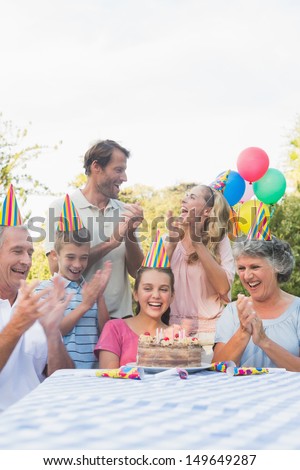 Cheerful extended family clapping for little girls birthday outside at picnic table