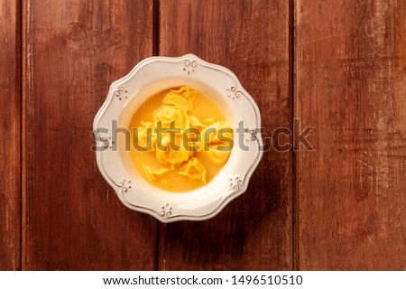 Italian tortellini served with broth, shot from the top on a dark rustic wooden background