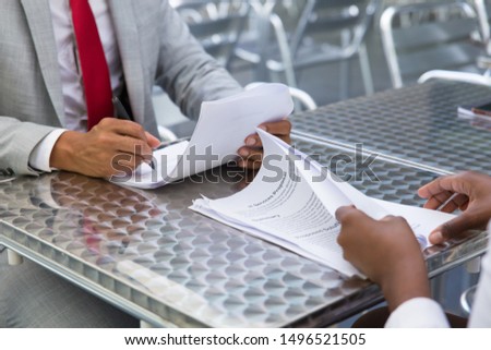 Business partners checking and signing documents in street cafe. Closeup of papers and writing business man hand. Deal or paperwork concept
