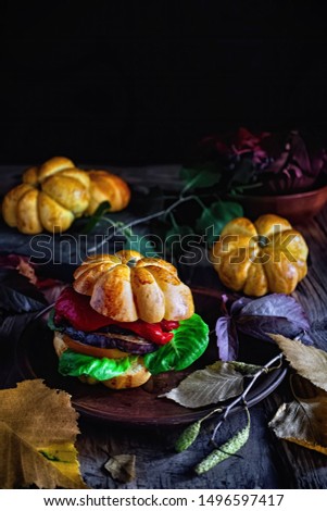 Homemade vegetable burger with pumpkin buns. Original baking in form of pumpkin in autumn leaves. Symbols and characters Halloween. Idea of design meal for Halloween party or Thanksgiving dinner.
