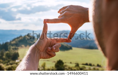 Rear view of Man looking at mountain landscape framing with fingers, searching for best image composition as he hiking over the mountain range. Landscape photographer or moviemaker occupation concept.