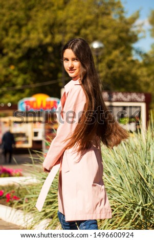 Portrait of a young beautiful brunette girl in pink coat on a background of autumn park