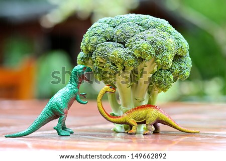 Funny picture of toy dinosaur eating broccoli tree. Photo can be used to help cooking with children, preparing kid-friendly dishes and promoting healthy food for children