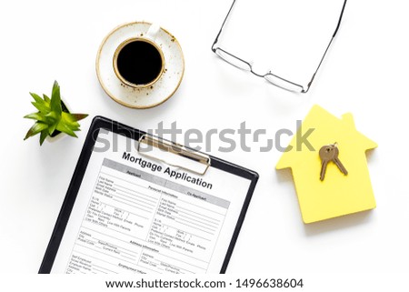 House mortgage with application, coffee, glasses, house toy, keys on white banker desk background top view