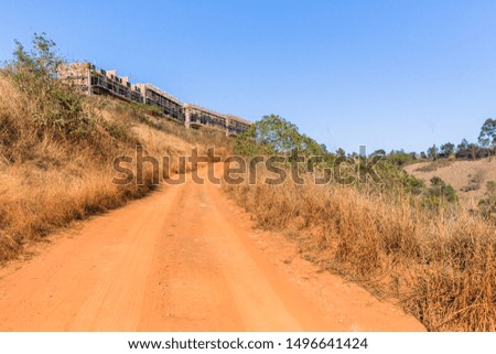 New building construction in progress  of flat apartments in rural countryside alongside dirt road dry grassland hills with blue sky.