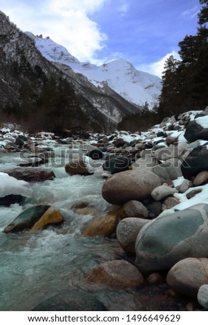 Mountain river among the big stones on the background of snow-capped peaks and blue sky. The Location Of Terskol,Elbrus district, Kabardino-Balkaria, Russia