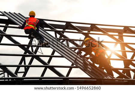 Construction engineer wear safety uniform using an electric drill and screw tools to fasten down metal roofing work for roof industrial concept with copy space Royalty-Free Stock Photo #1496652860