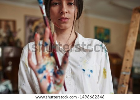 Focused photo. Holds brush. Young creative woman is in art studio. Conception of painting.