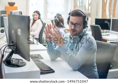 Young handsome male technical support agent trying to explain something to a client while using hands-free headset at call center Royalty-Free Stock Photo #1496751047