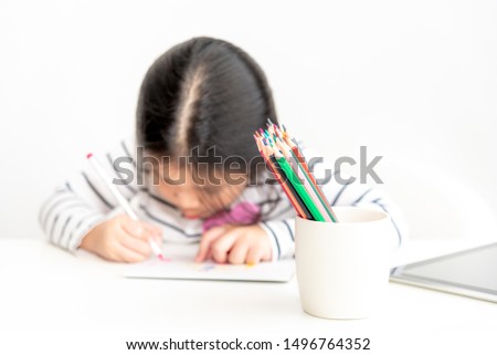 Blurred images of A 6 year old Asian girl are concentrating on making card for mothers on important occasions On white background, concept to children and education. This picture focuses on pencils.