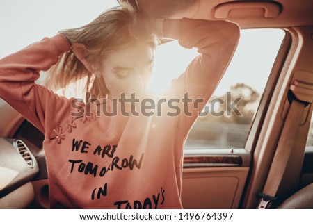 Beauty portrait of pretty girl in car on parking in evening. Stylish urban woman model posing in red hoodie in summer sunset Royalty-Free Stock Photo #1496764397