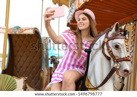 Young pretty woman taking selfie on carousel in amusement park