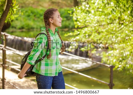 Emotional girl teenager with long hair hairstyle braids in a green shirt walks in the park at the waterfall on a sunny day.
