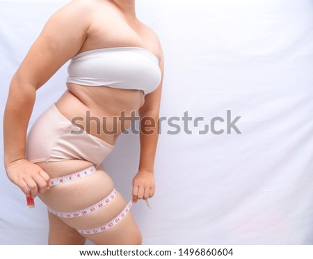 A beautiful fat woman with a tape measure, she uses her hand to hold the tape measure to measure her legs on a white background. She wants to lose weight the concept of surgery and break down the fat  Royalty-Free Stock Photo #1496860604