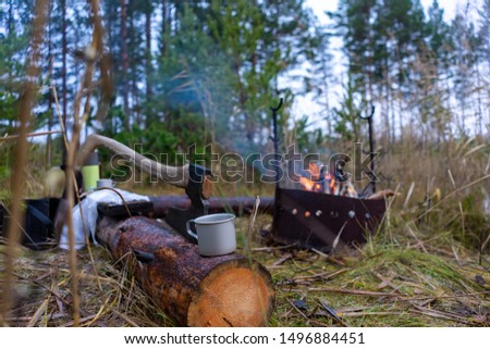 camp travelers in the woods with a burning fire, an ax and a mug of tea