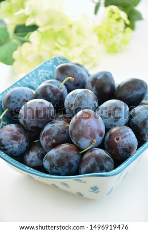 Fresh picked organic prune plums in decorative bowl on white background in vertical format.  Selective focus. Healthy food concept.