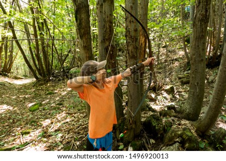 Boy shooting with a bow and arrow in the forest Royalty-Free Stock Photo #1496920013