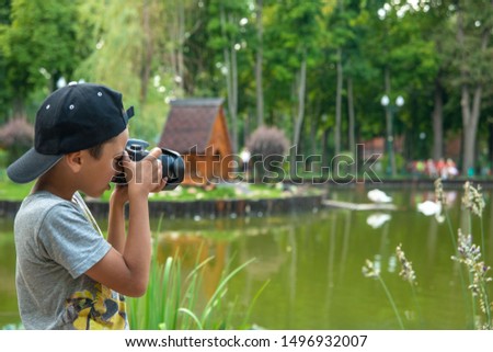Young boy photographs scenic spots in the park.  He stands by the lake and takes pictures of swans.