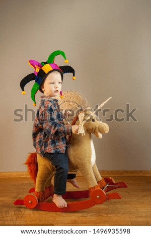 Funny boy in plaid shirt with toy sword and shield made of straw sits on rocking horse. Boy dreams of battles, victories and adventures. Concept of education morale, patriotism, strength of mind