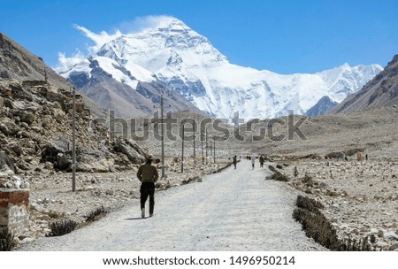 Cinematic shot of travelers hiking down the empty gravel trail and towards the breathtaking windswept Mount Everest on a sunny day. Fit explorers trekking to the foothills of snow covered Everest.