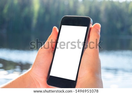 Mobile phone in hand, isolated with white screen, against the background of nature and pond