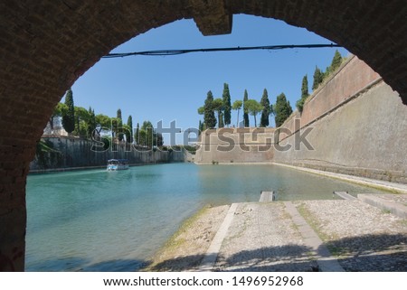The bottom view from under the bridge is the water of Lake Garda, in the distance is a boat, trees. Peschiera del Garda. Place for writing text