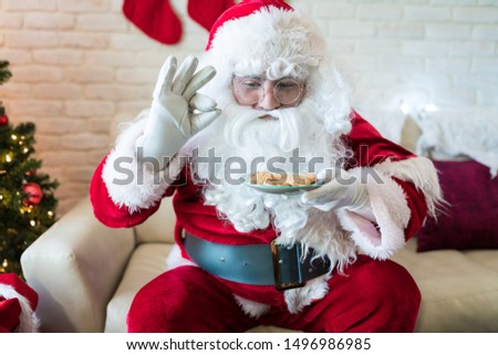 Santa Claus enjoying his cookies while sitting on sofa at home during Christmas