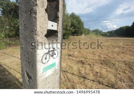 horizontal closeup photography of a green bike trail sign on a concrete electric pole, with a field in a background, outdoors in a summer in POland, Europe