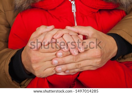 Close up picture of young couple holding hands, wearing red and brown winter coat