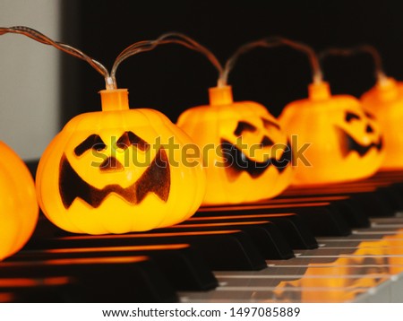 Electric string Halloween pumpkin lights decorated on piano keyboard background for happy Halloween party in October month.