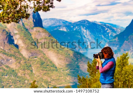 Tourist woman taking with camera travel picture, enjoying fjord mountains landscape. National tourist scenic route Aurlandsfjellet in Norway