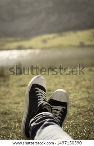 Vertical grunge picture of a close-up of a blue and white pair of shoes relaxing on a green meadow with a defocused lake in the background