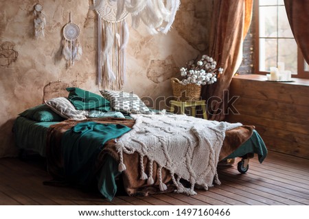 Stylish room interior with large comfortable bed. Beige and white dream catchers and feathers hanging above gypsy or hippie slyle bed in dark autumn bedroom interior Royalty-Free Stock Photo #1497160466