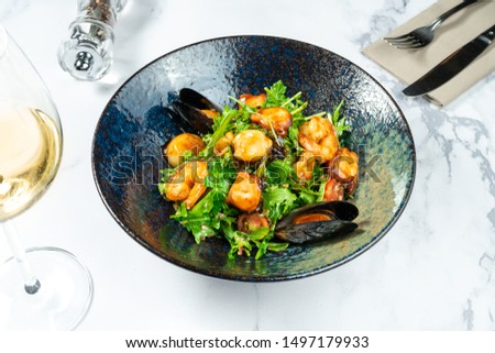 Warm seafood salad in a stylish black bowl on a marble table. Scallop salad. mussels, shrimps in sweet and sour sauce. Healthy and balanced food for dieting. Restaurant style food