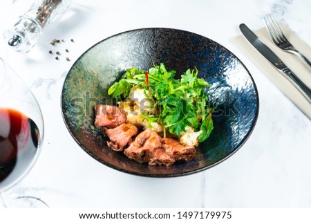 Warm salad with roast beef, crackers, arugula and sauce in a black bowl on a marble table served with red wine. Tasty and healthy snack for lunch. Food photo background